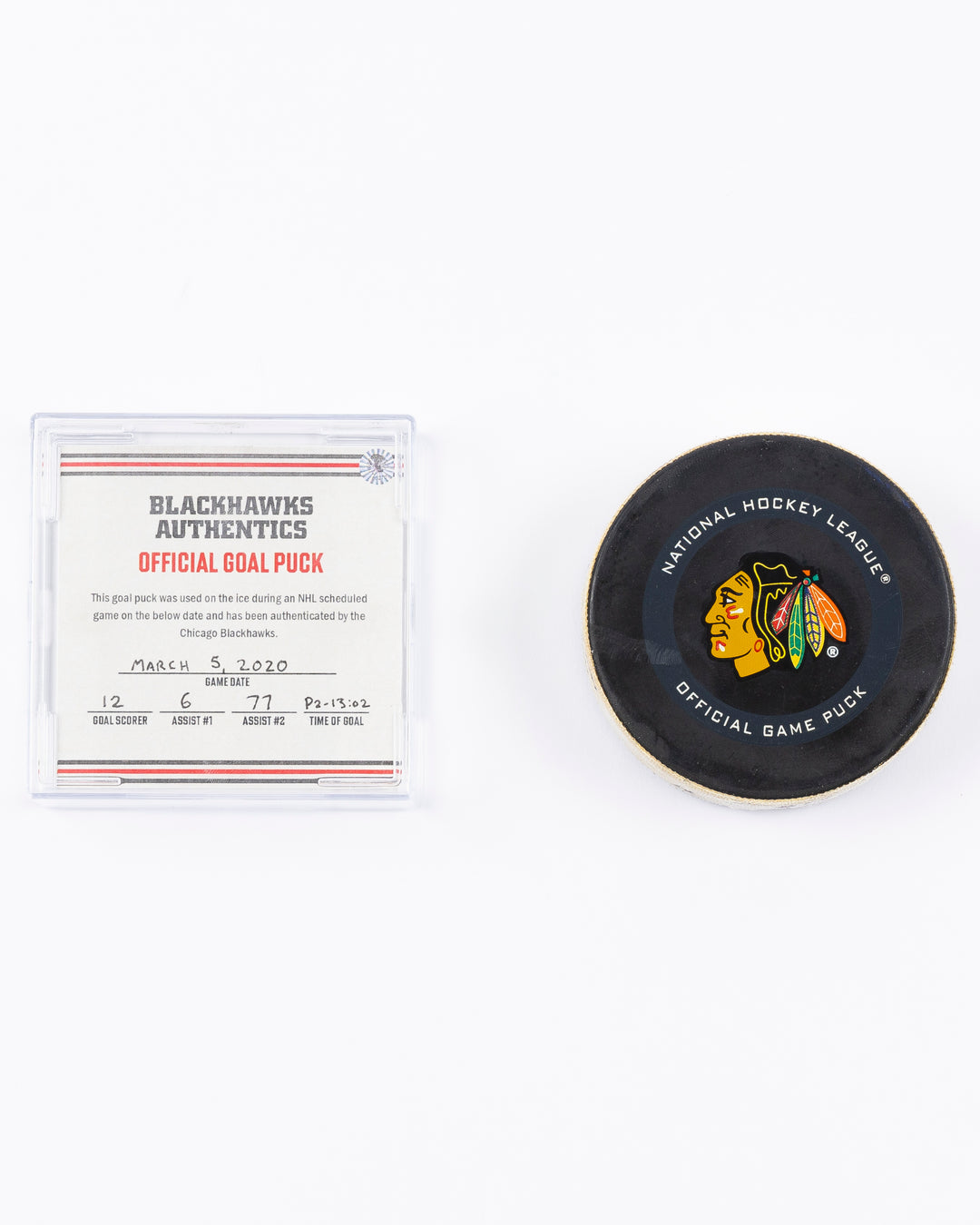 game-used hockey goal puck shot by former Chicago Blackhawks player Alex DeBrincat - front and card lay flat