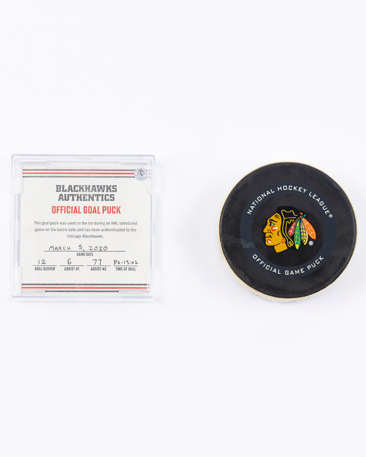 game-used hockey goal puck shot by former Chicago Blackhawks player Alex DeBrincat - front and card lay flat