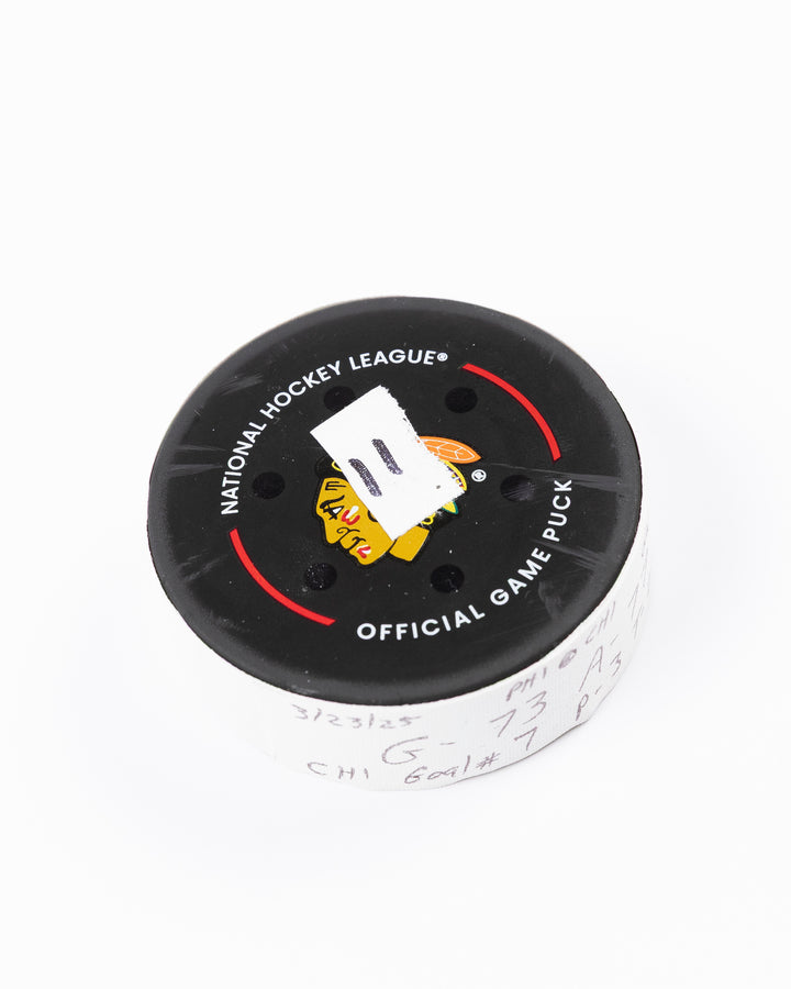 official game used hockey goal puck used by Chicago Blackhawks player Lukas Reichel - front angle lay flat