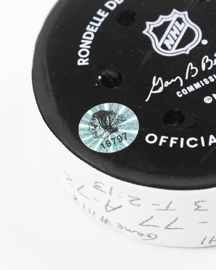 official game used hockey goal puck used by Chicago Blackhawks player Lukas Reichel - hologram sticker detail lay flat