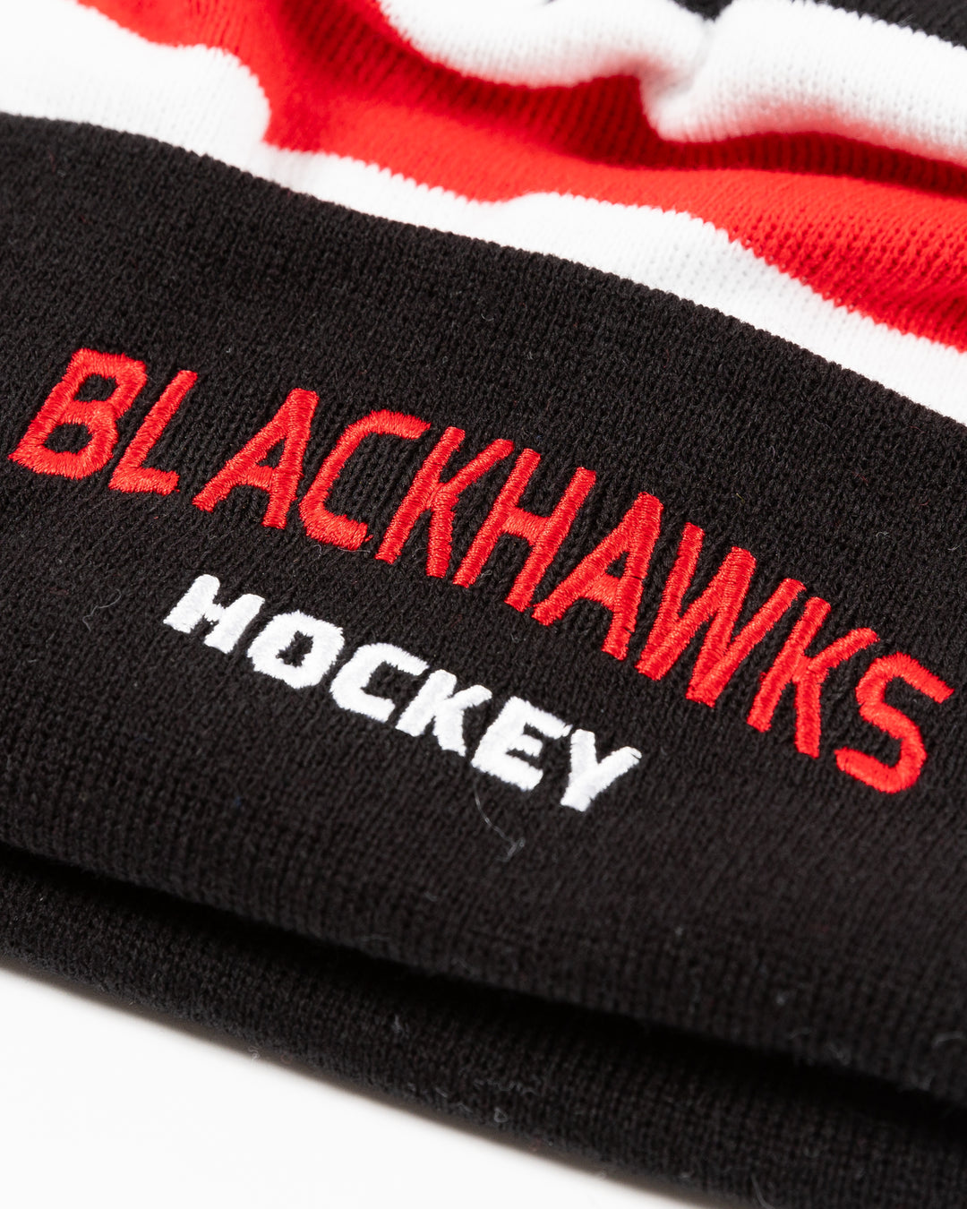 black CCM knit beanie with red and white stripe on front and embroidered Blackhawks Hockey wordmark on front cuff with multicolor pom on top - front detail lay flat