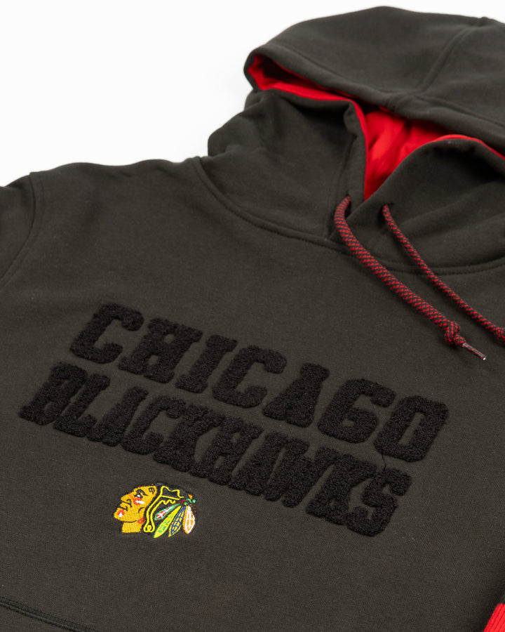 black New Era hoodie with Chicago Blackhawks chenille word graphic on front above embroidered primary logo with red stripes on sleeves - front detail lay flat