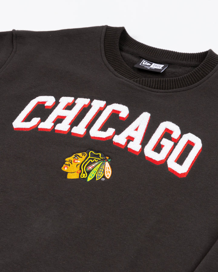 black New Era crewneck pullover sweater with Chicago wordmark in chenille above embroidered Blackhawks primary logo on front - front detail lay flat