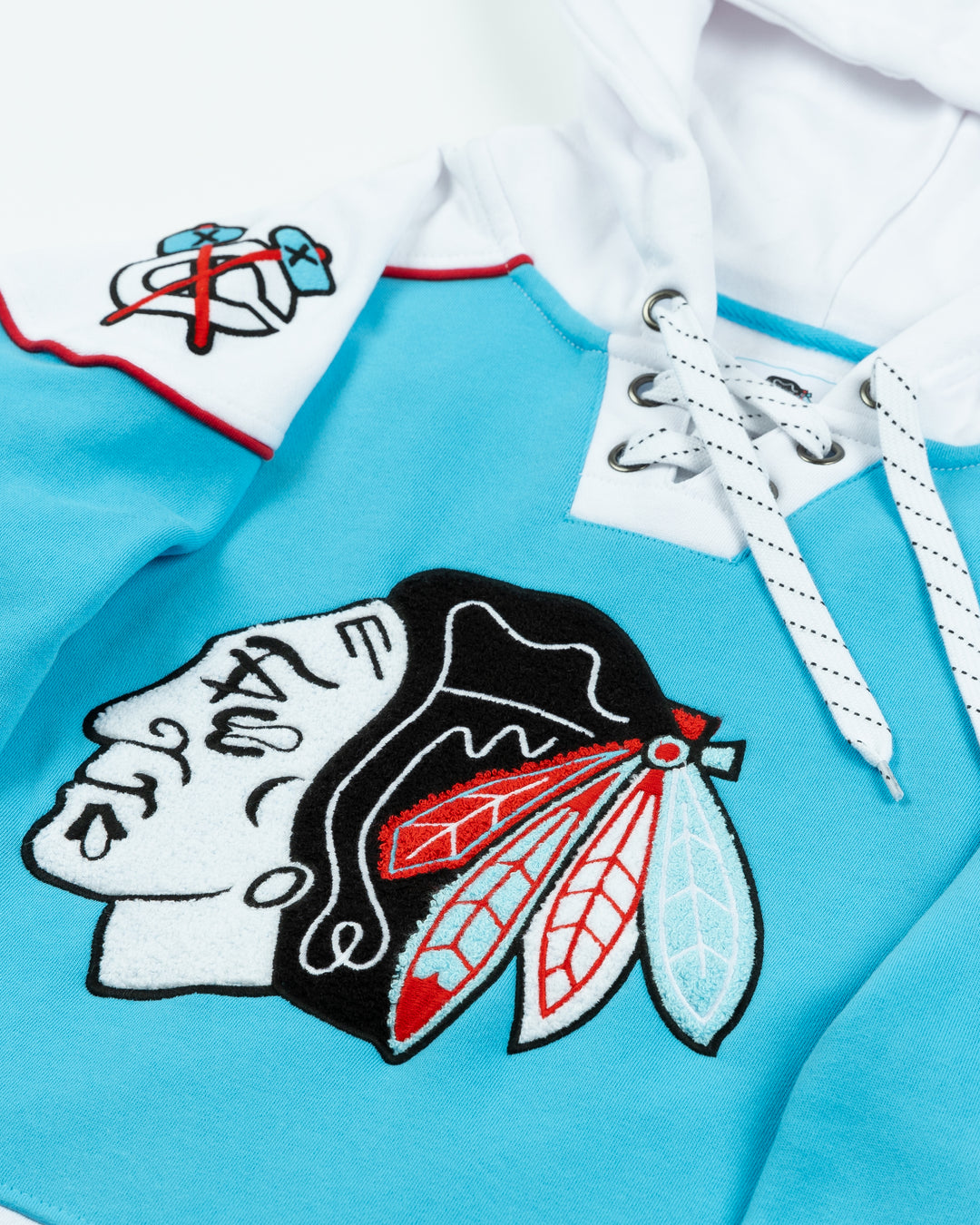 blue, white and red lace up hockey jersey hoodie with Chicago Blackhawks primary logo in Chicago flag-inspired colorway and secondary logos embroidered on shoulders - front detail lay flat