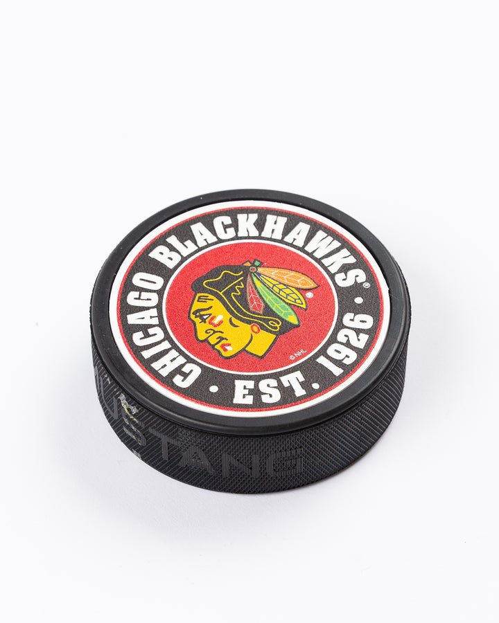 hockey puck with Chicago Blackhawks primary logo and established 1926 word graphic surrounding it - front angle lay flat
