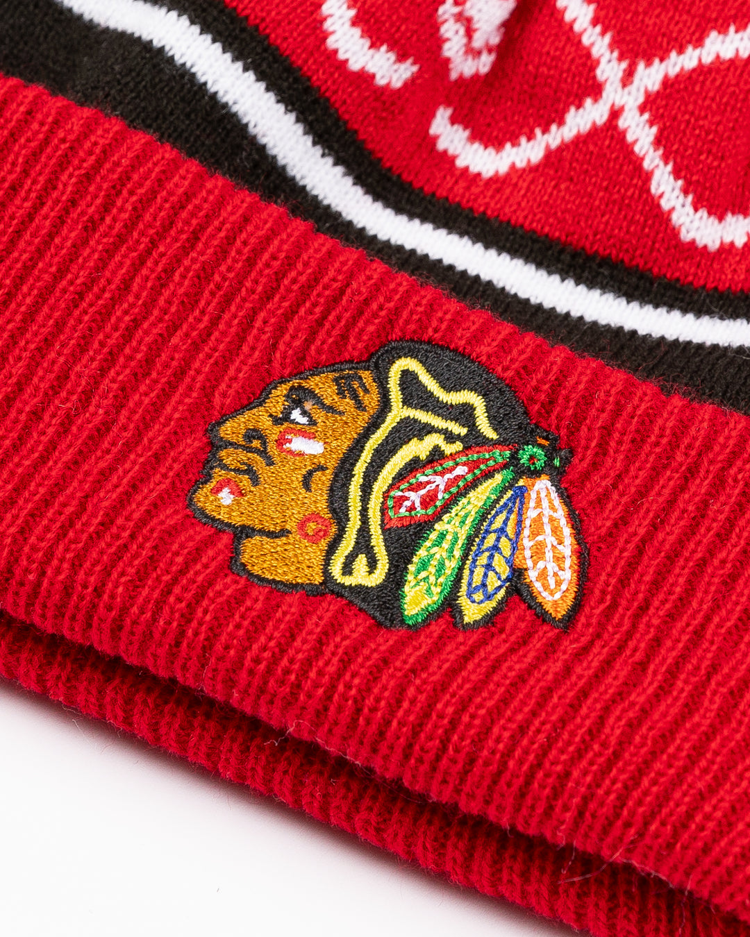 red white and black infant sized knit beanie with red and white pom and hockey stick and puck graphic with Chicago Blackhawk primary logo embroidered on front cuff - front detail lay flat